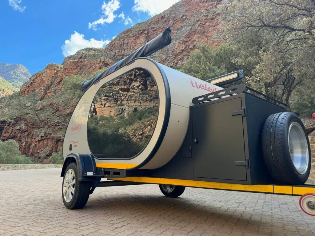 A Naledia Camper shown parked and shot somewhat from a low angle to show the trailers frame and integrated awnings.