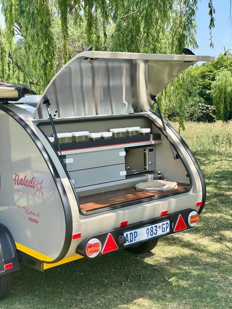 The rear kitchen of a Naledi Camper shown with the hatch open to reveal the kitchen's storage area, counter, microwave and other features. 