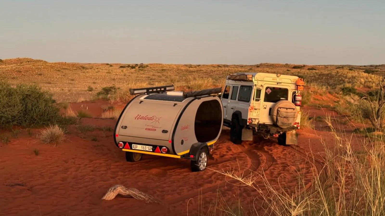 A Naledi Teardrop Camper parked in the African Plains next to a classic Land Rover Defender 110 in white