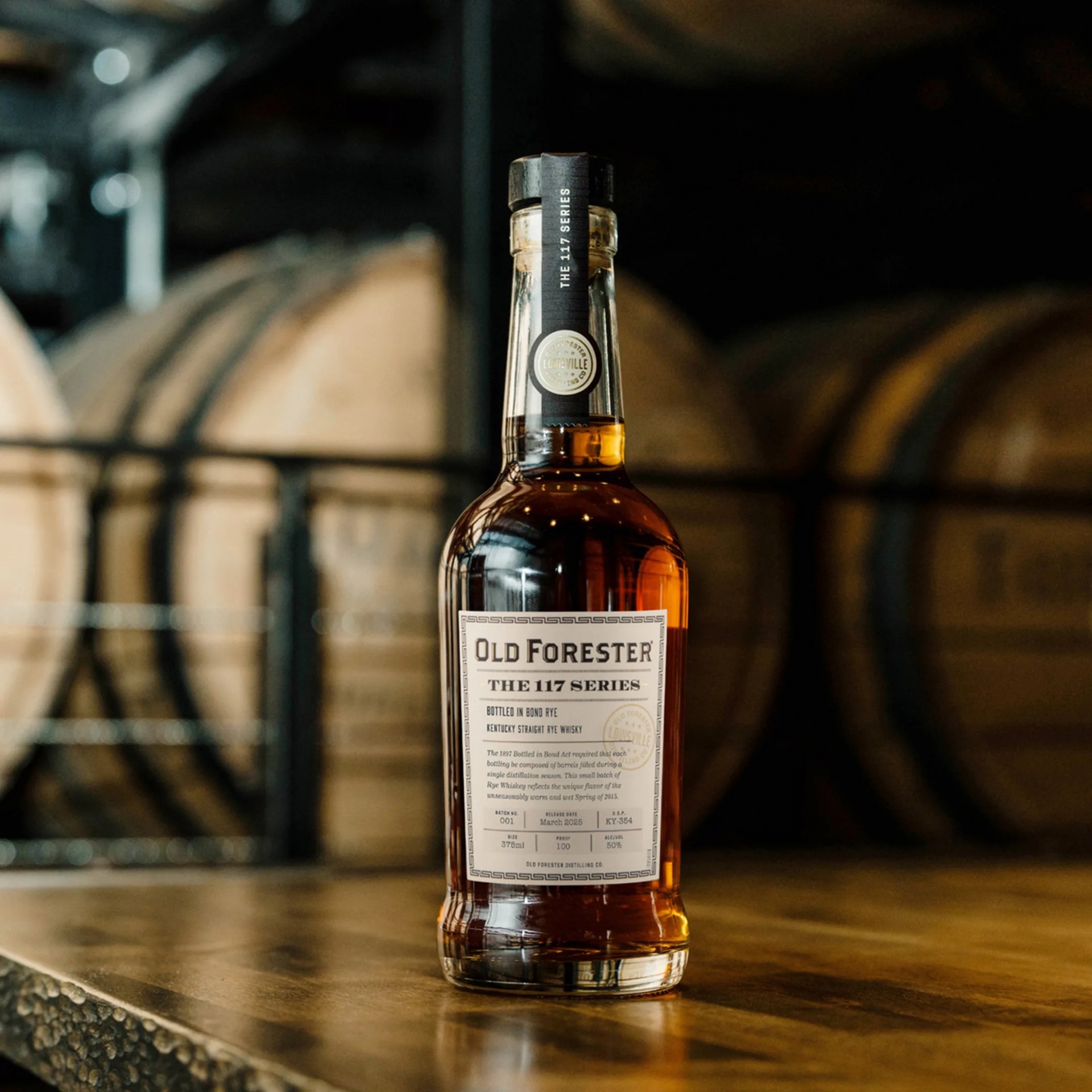 Old Forester 117 Bottled in Bond Rye Whiskey in front of barrels on table