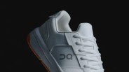 A close up of the heel of the ON THE ROGER Clubhouse revised sneaker. The sneaker is white with a tan colored gum sole and shown against an all-black background.