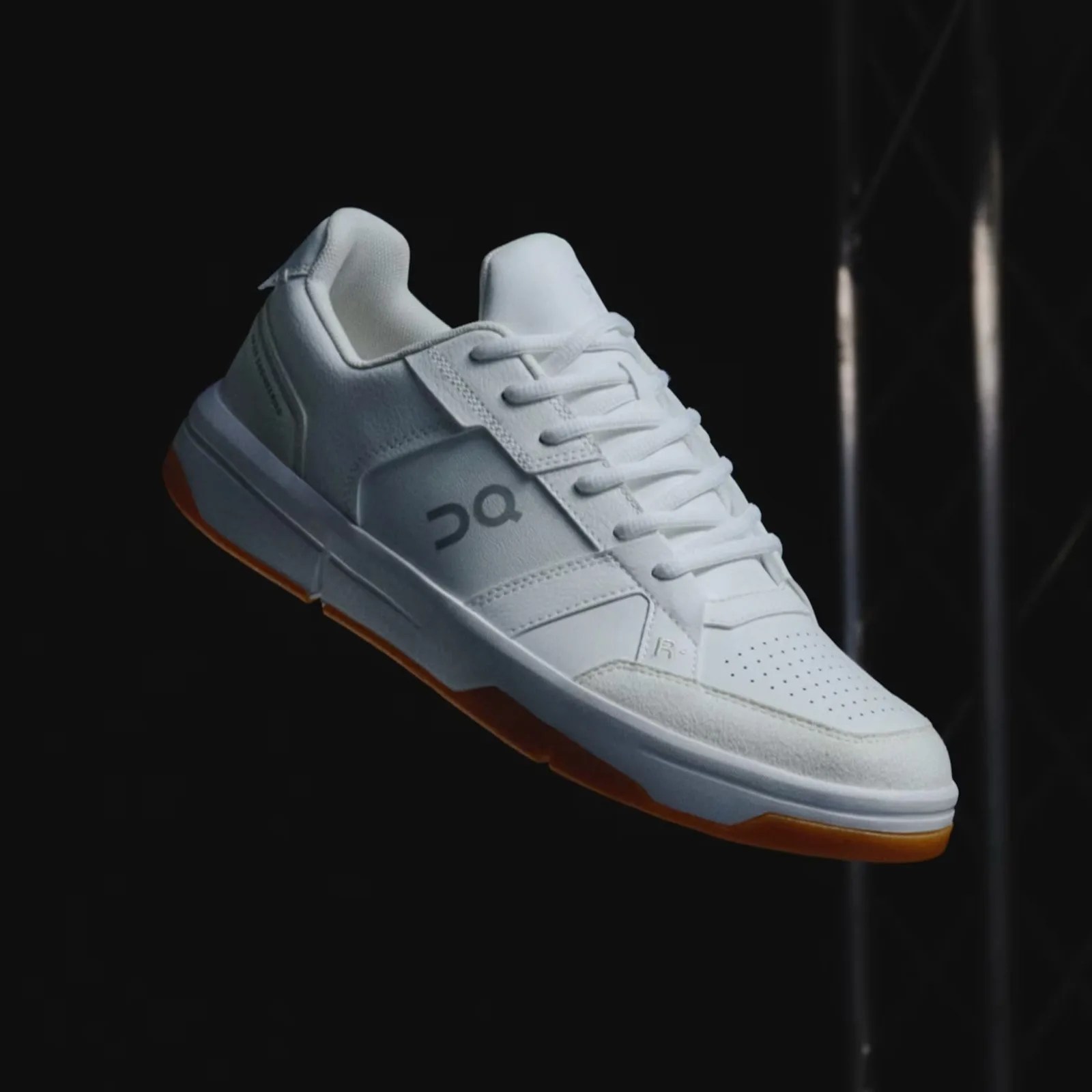 A single On THE ROGER Clubhouse revised sneaker in white and ivory floating in the air in an angle against a dark black background
