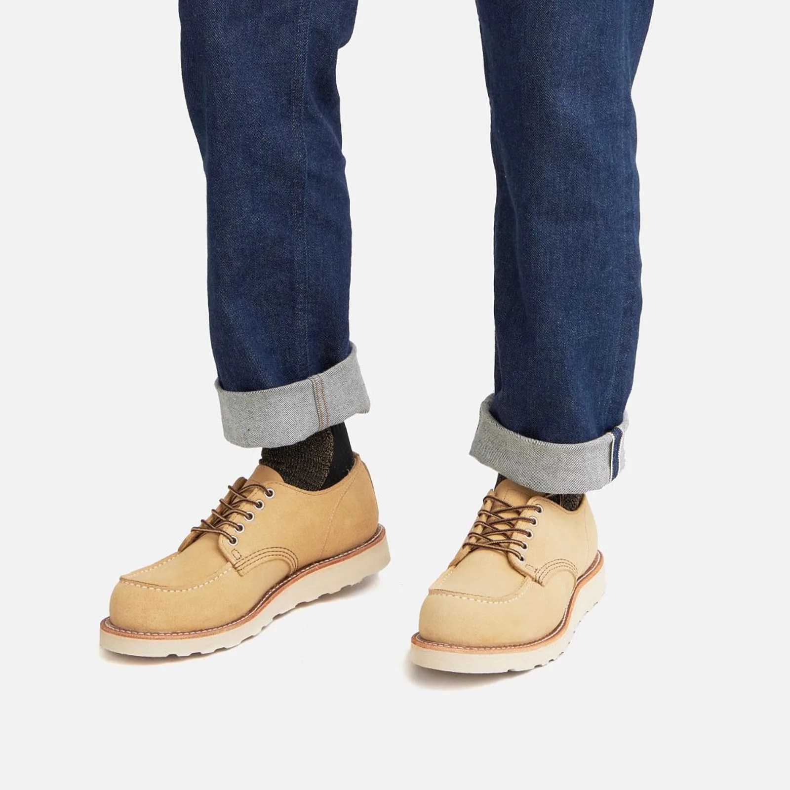 A pair of Red Wing Heritage Shop Moc Oxfords shown in a new yellowish-tan Hawthorne colorway. The low-cut shoes are shown on a male model wearing cuffed dark blue jeans. The picture is taken from just below the knees down. 