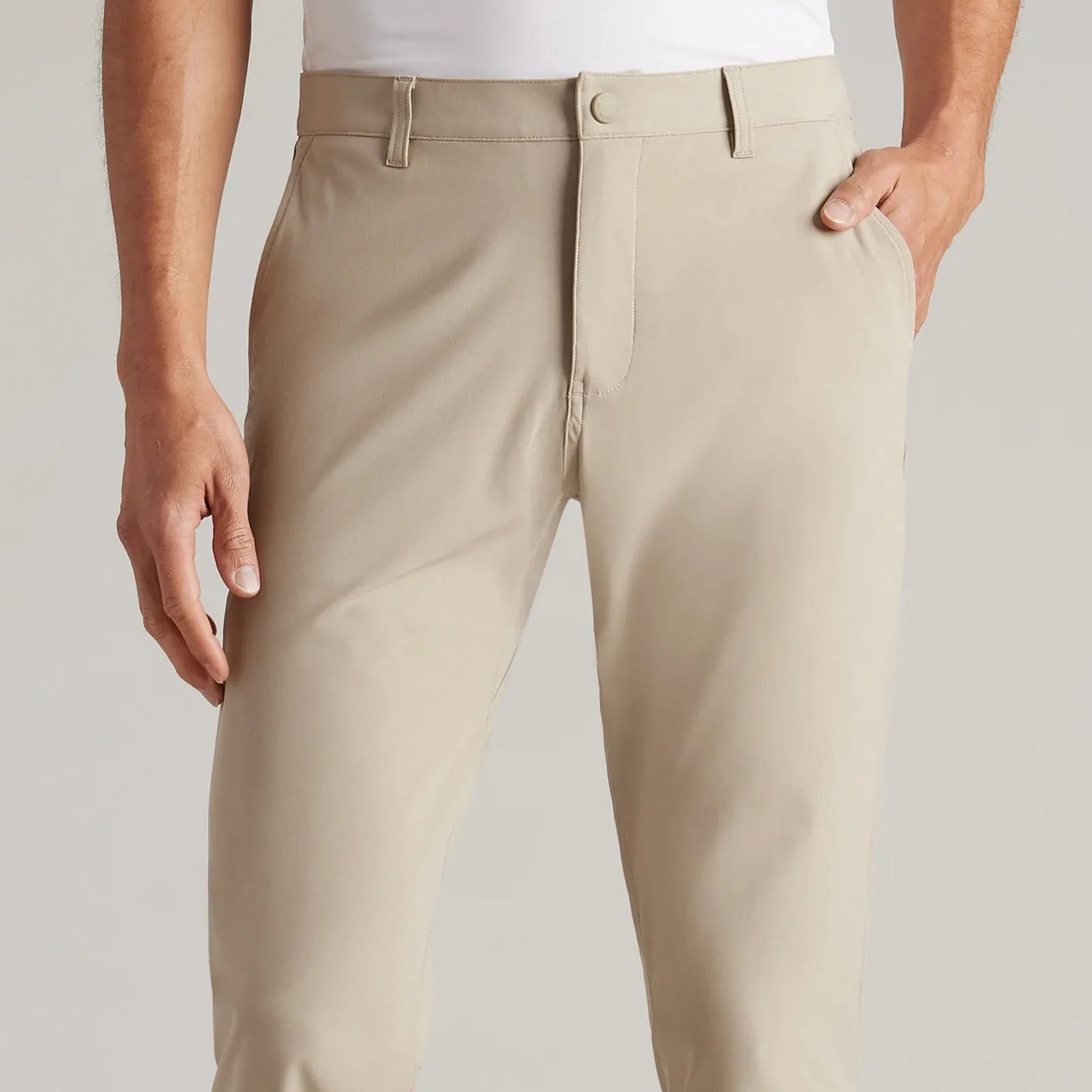 A view of the button front of the Rhone Commuter Pant in light khaki is shown being worn on a light-skinned model from the waist to the upper knee area