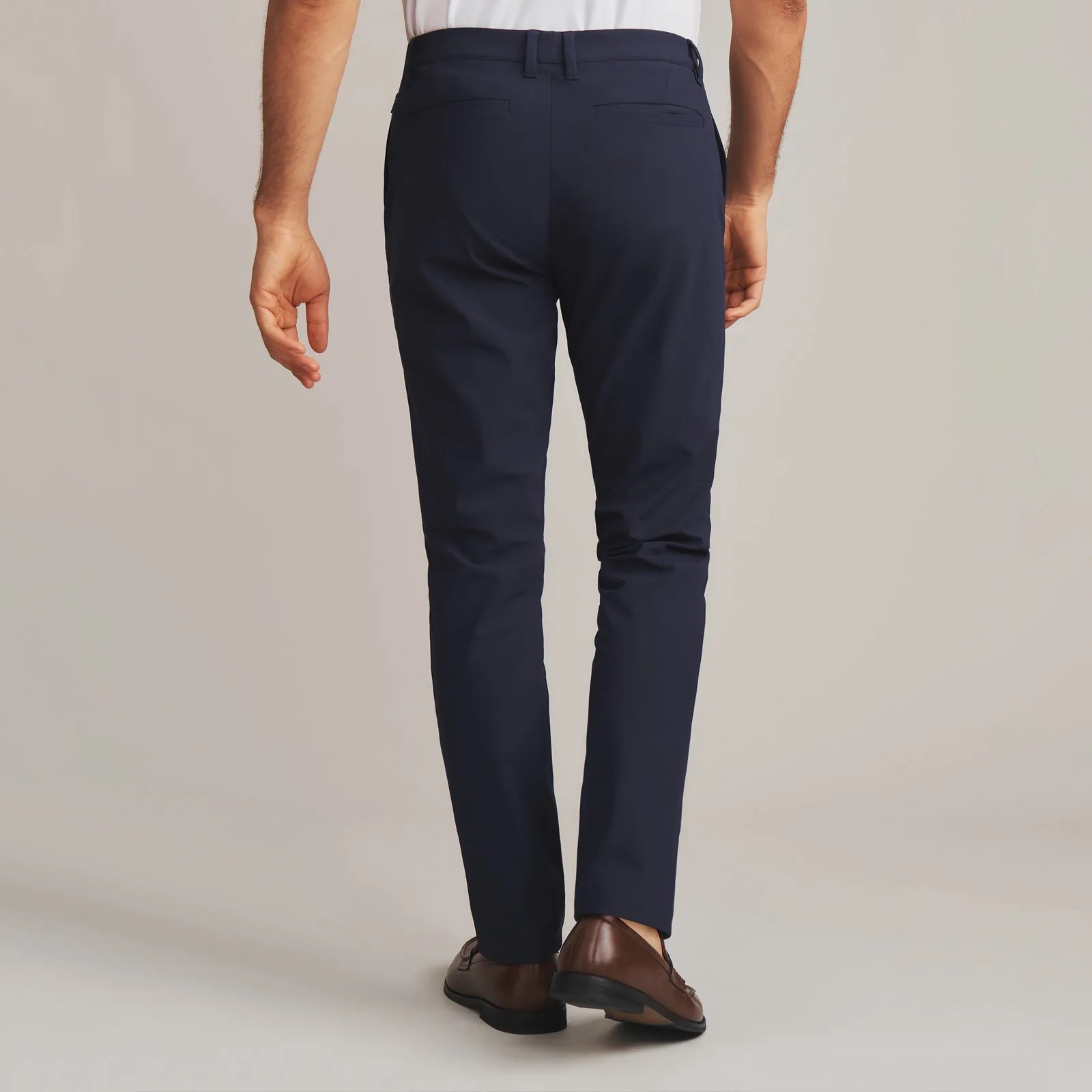 A pair of navy Rhone Commuter Pro Pants shown from behind on a male model from the waist down. 