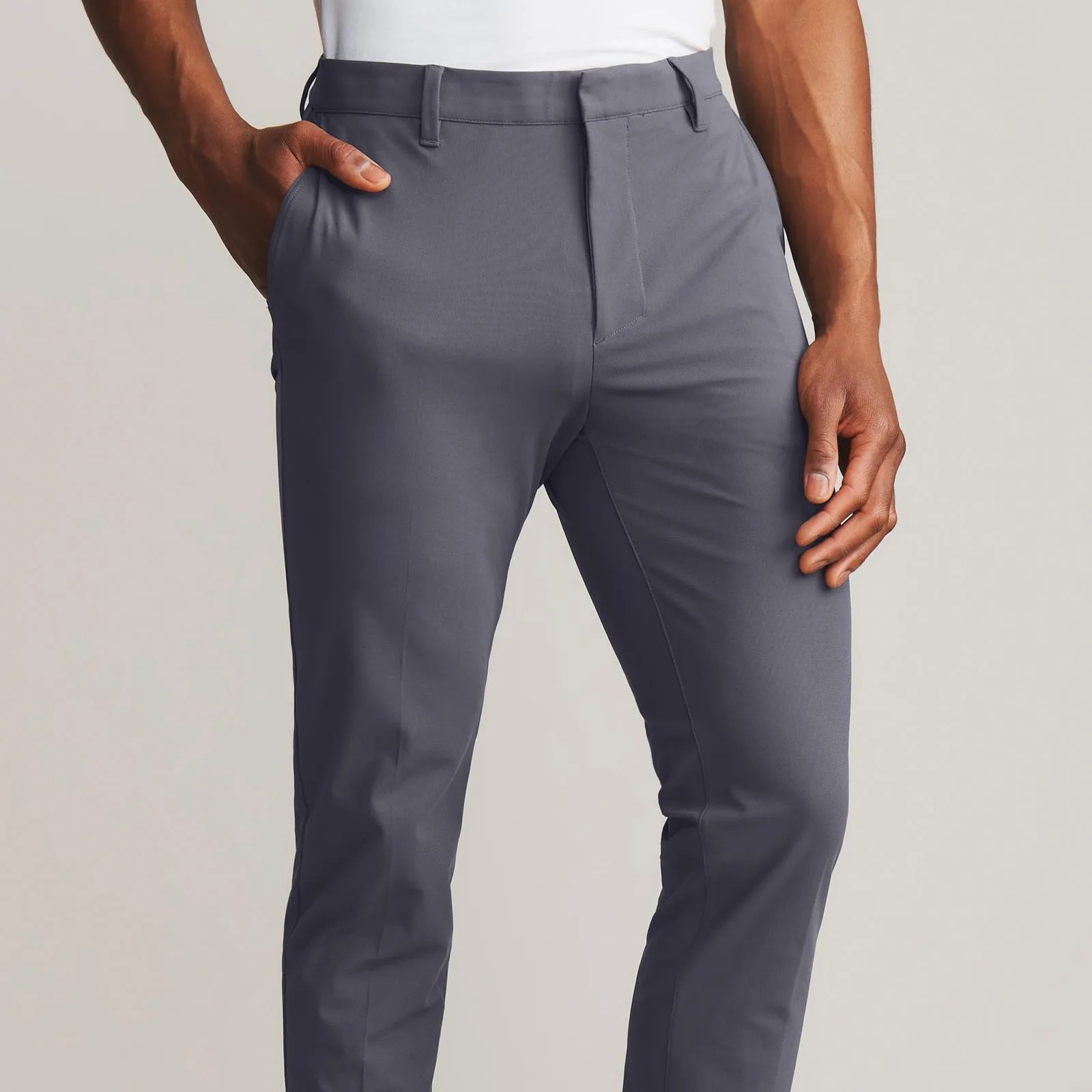 A view of the button-less front closer of the Rhone Commuter Pant Pro in grey is shown being worn on a dark-skinned model from the waist to the shin area. 