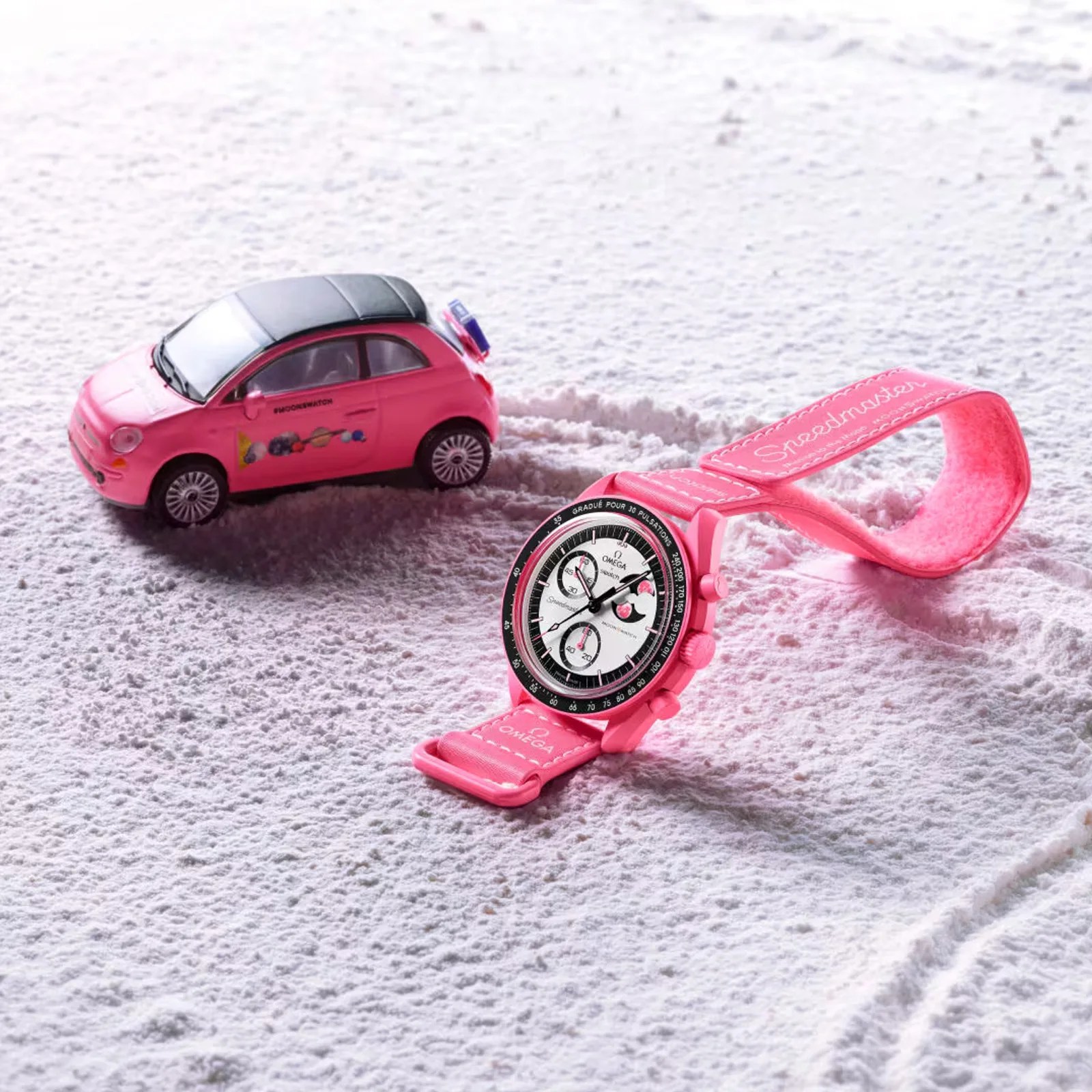 The MoonSwatch Mission to the Pink Moonphase  shown siting on what looks like the lunar surface next to a pink MoonSwatch branded car that appears to be the same size as the MoonSwatch