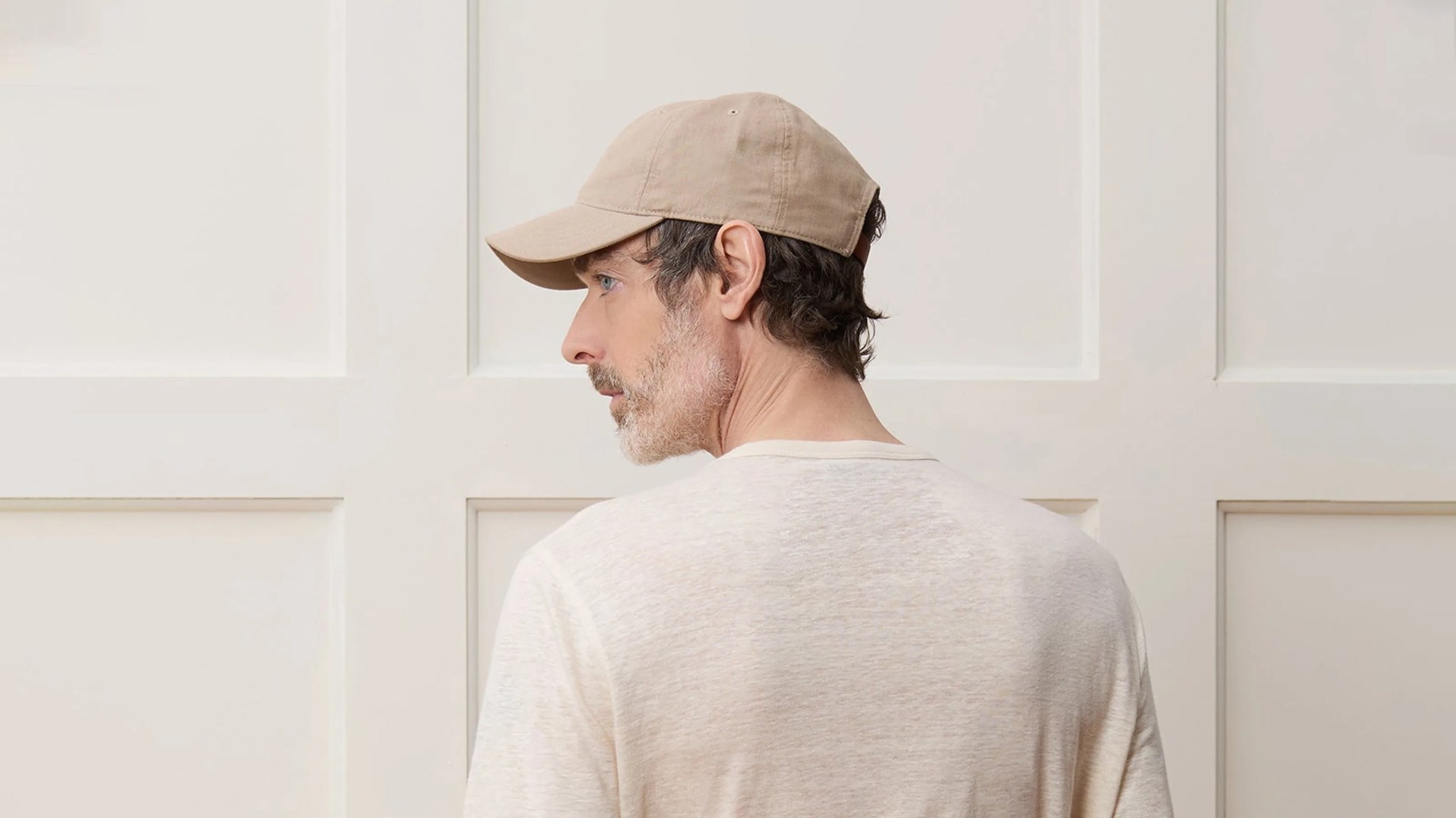 A white male is shown from behind, looking to the left, wearing a light tan Todd Snyder baseball hat. In background