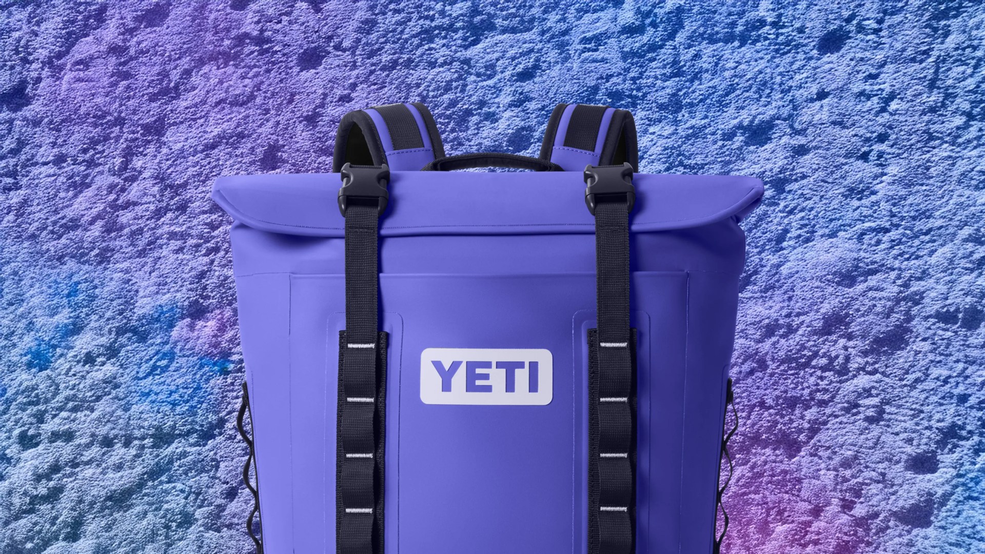 A Yeti hooper back pack cooler shown in a purplish blue color called Ultramarine. The background is a blueish purplish coral reef pattern
