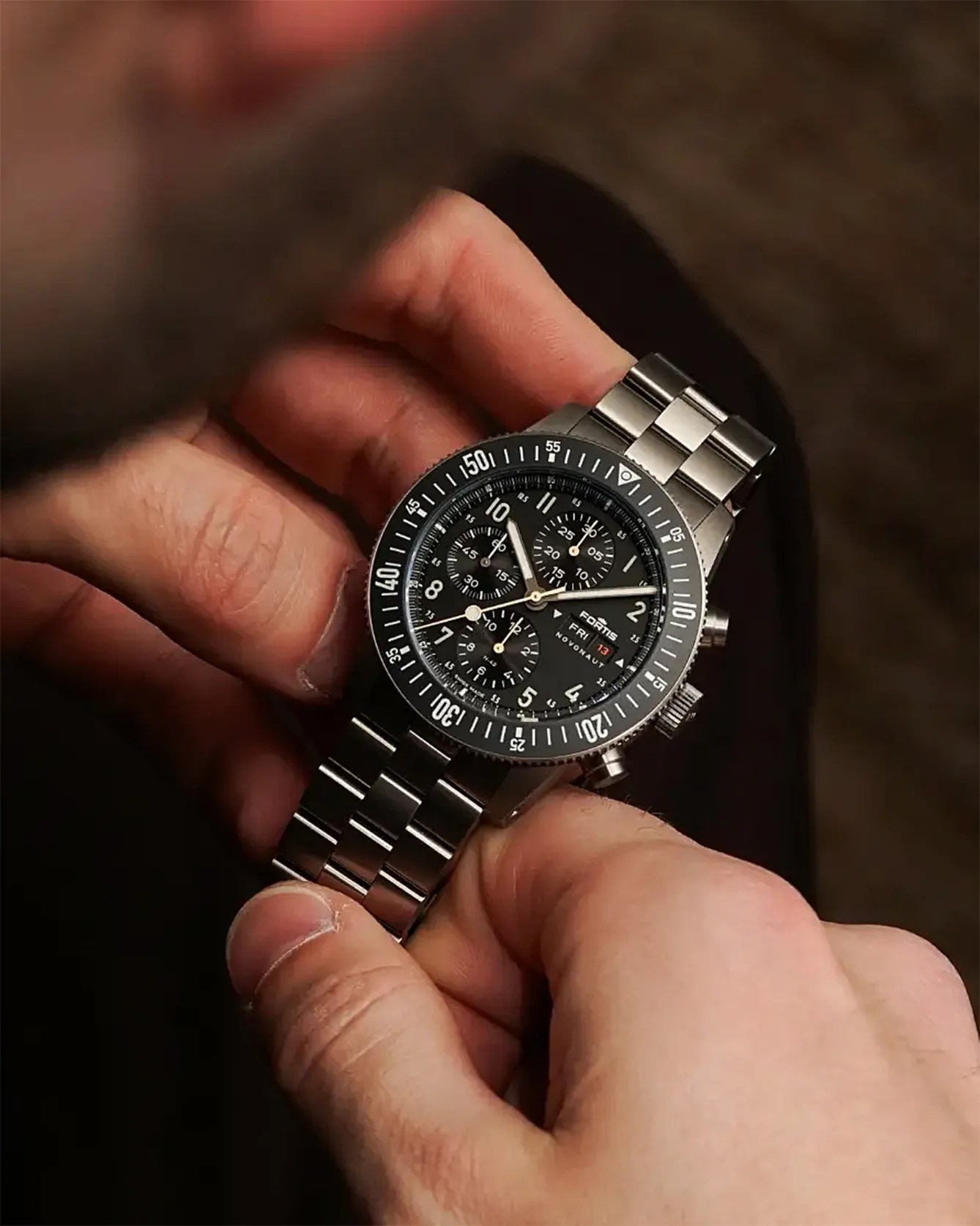 a man holding a steel chronograph watch with a back dial