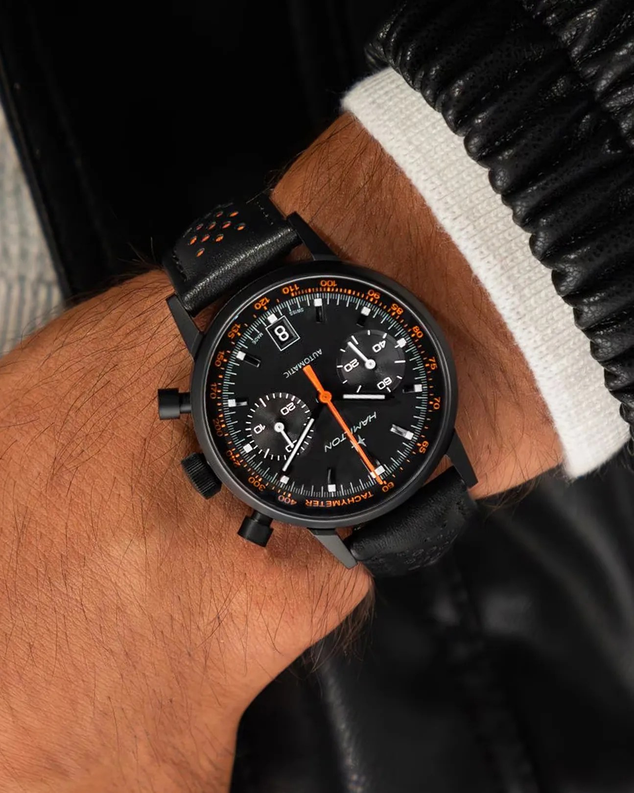 a black chronograph watch with orange details on a man's wrist