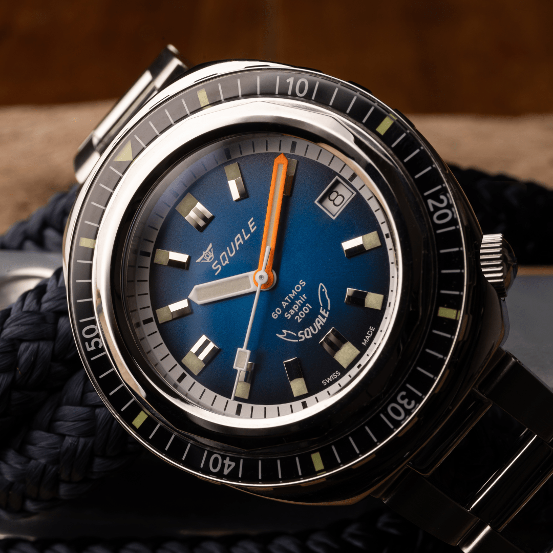 The Squale 2001 dive watch has a blue face and is shown resting on one side of the face on top of a pile of nautical rope. 