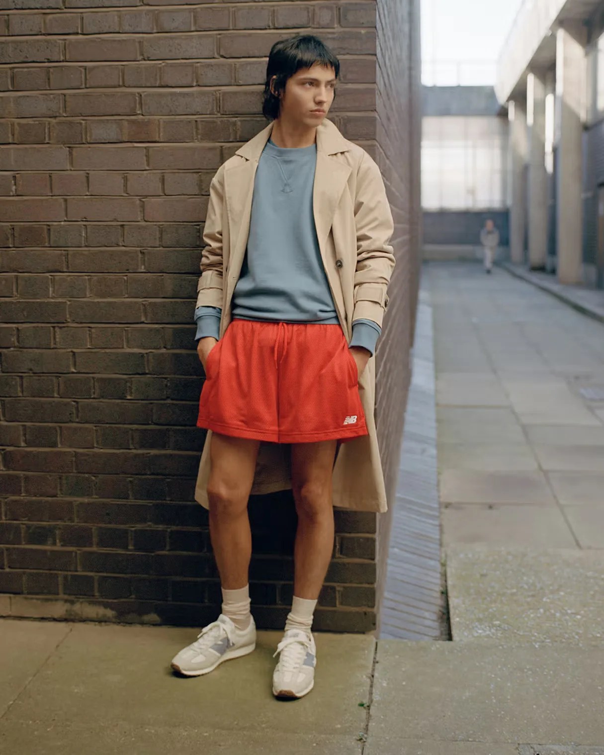 a man wearing a pair of white New Balance running shoes, red shorts, and a trench coat