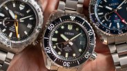 three steel dive watches in a man's hand