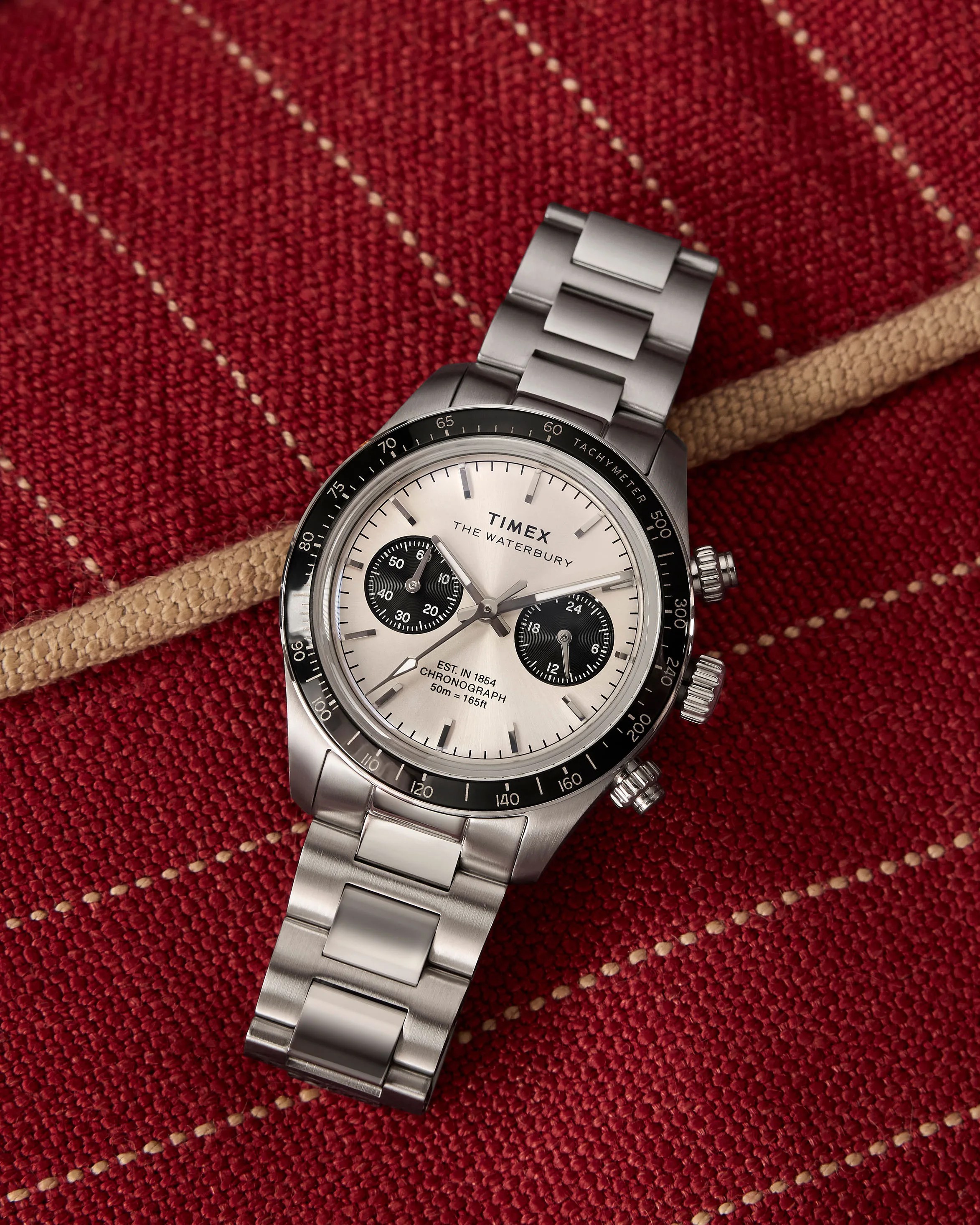 a steel Timex chronograph watch laying on a red couch