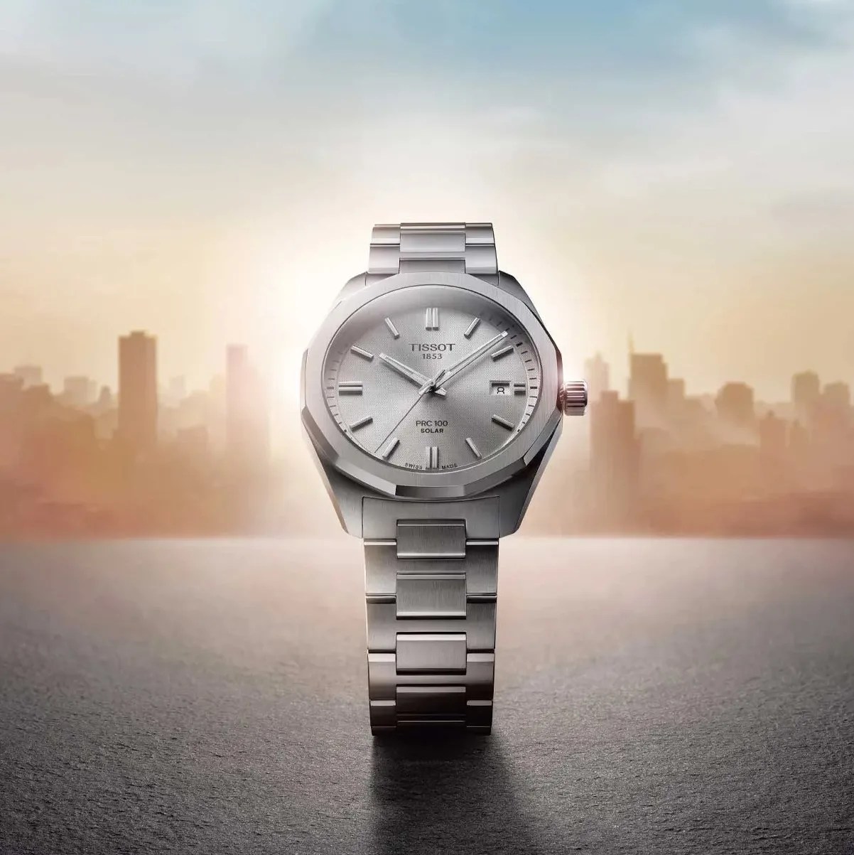 a steel Tissot watch with a silver dial and a sunrise in the background