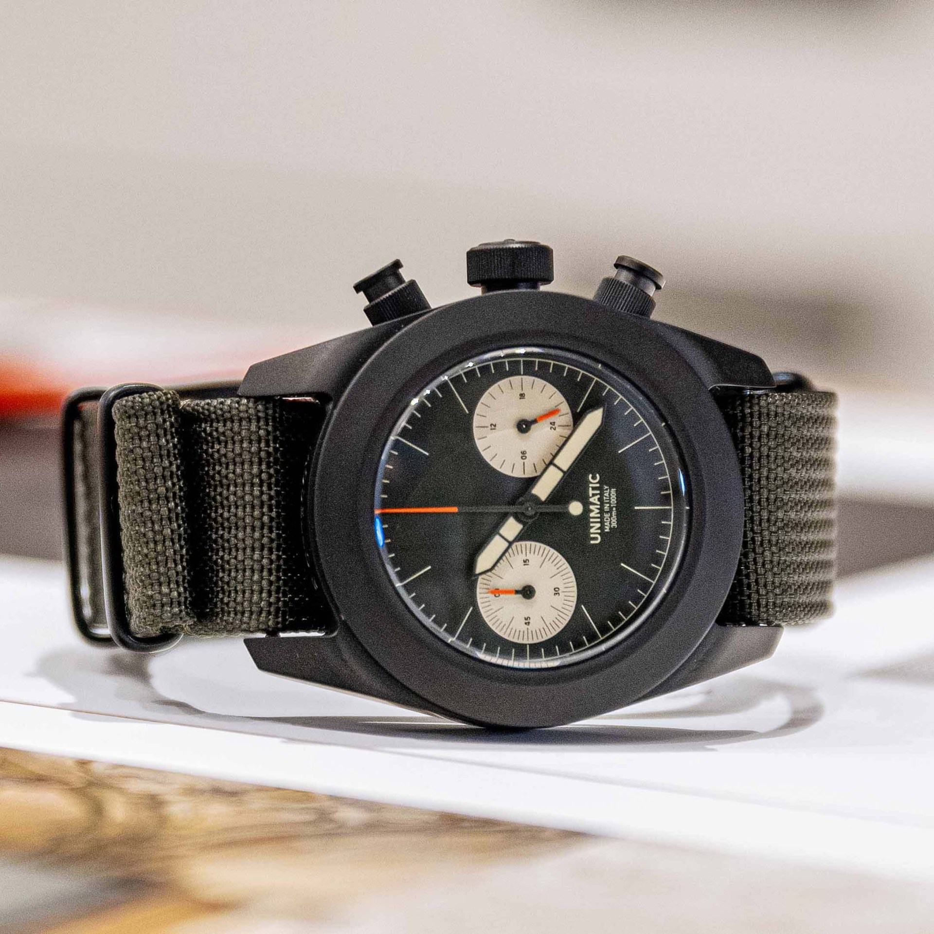A black chronograph watch with an olive strap