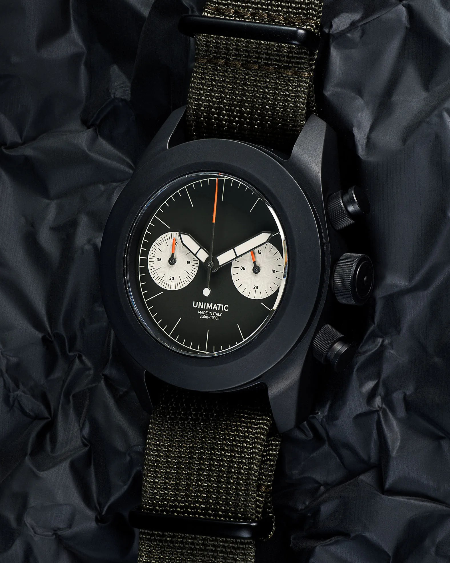 a black chronograph watch laying on a black tarp