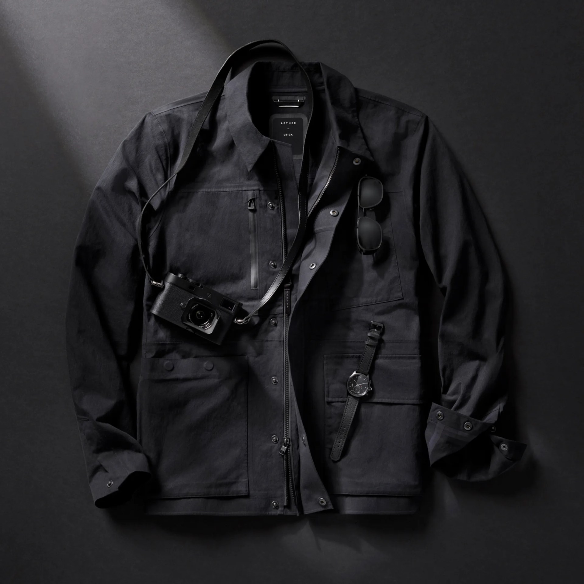 Aether x Leica Reporter Jacket with camera, watch and sunglasses