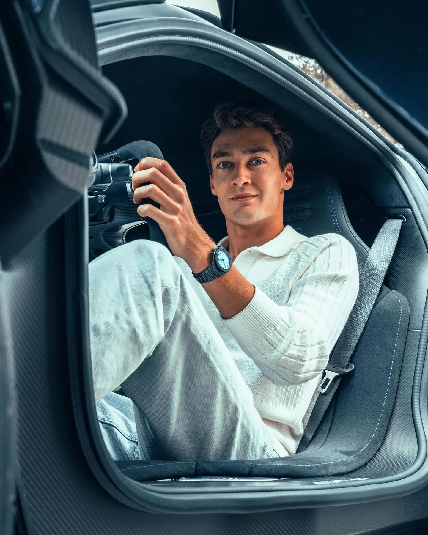 F1 Driver George Russell shown behind the wheel wearing a Mercedes supercar steering wheel, showing his custom Ingenieur Automatic 42 in black ceramic with a custom blue face. 