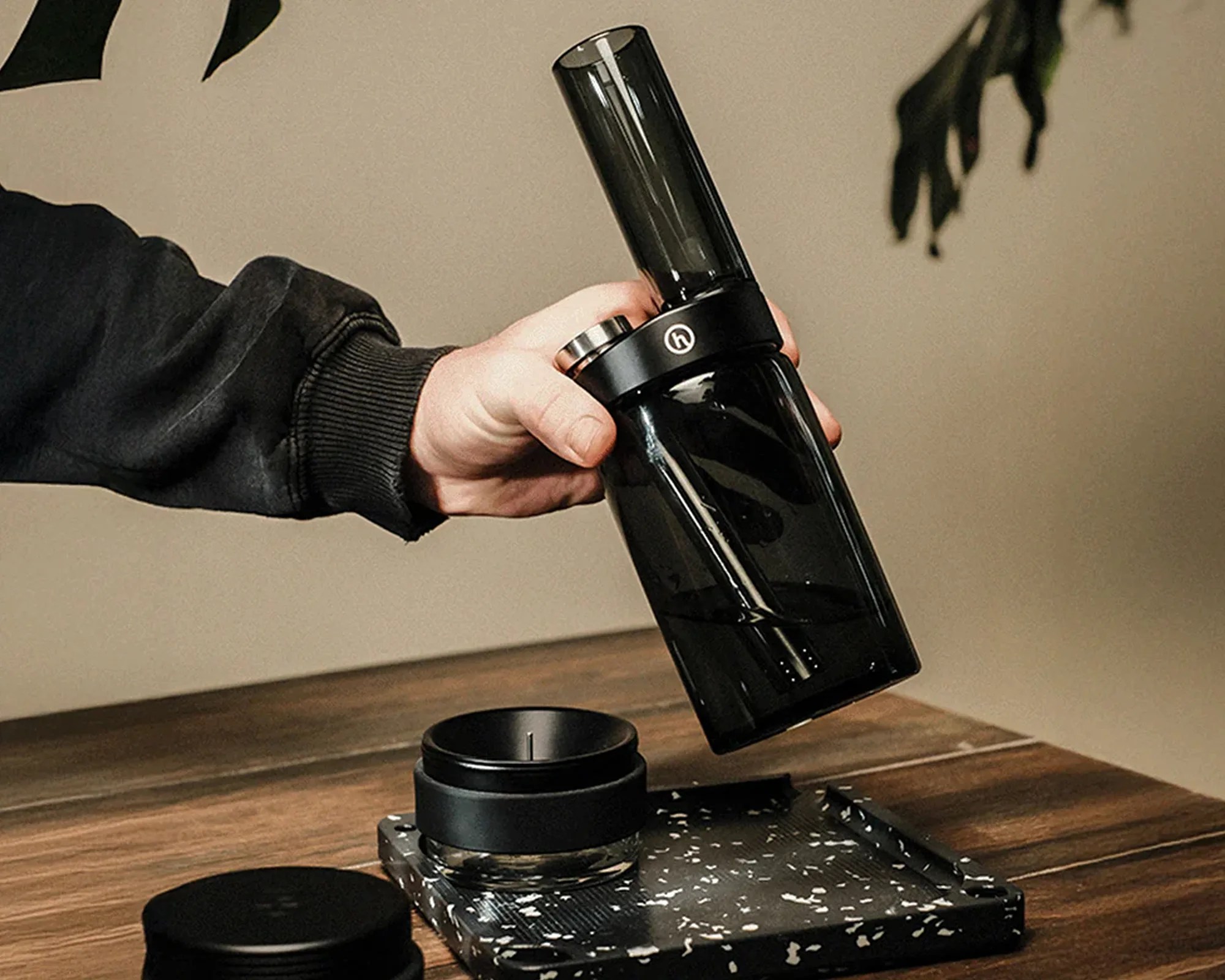 Honest Smoked Capsule bong in hand above rolling tray, ash tray and wooden table