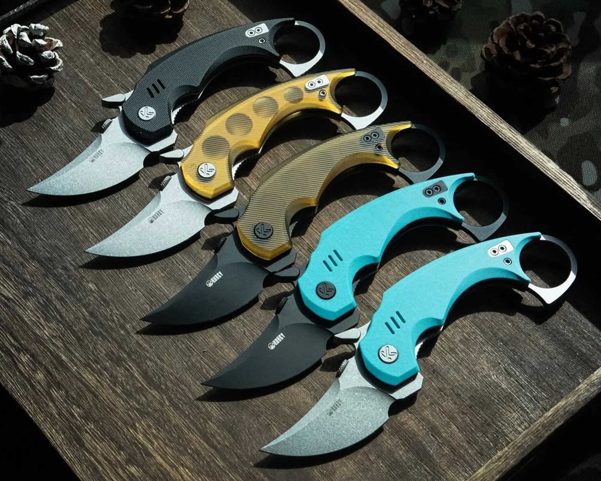 Kubey Jaw Folding Karambit knives on wooden valet tray