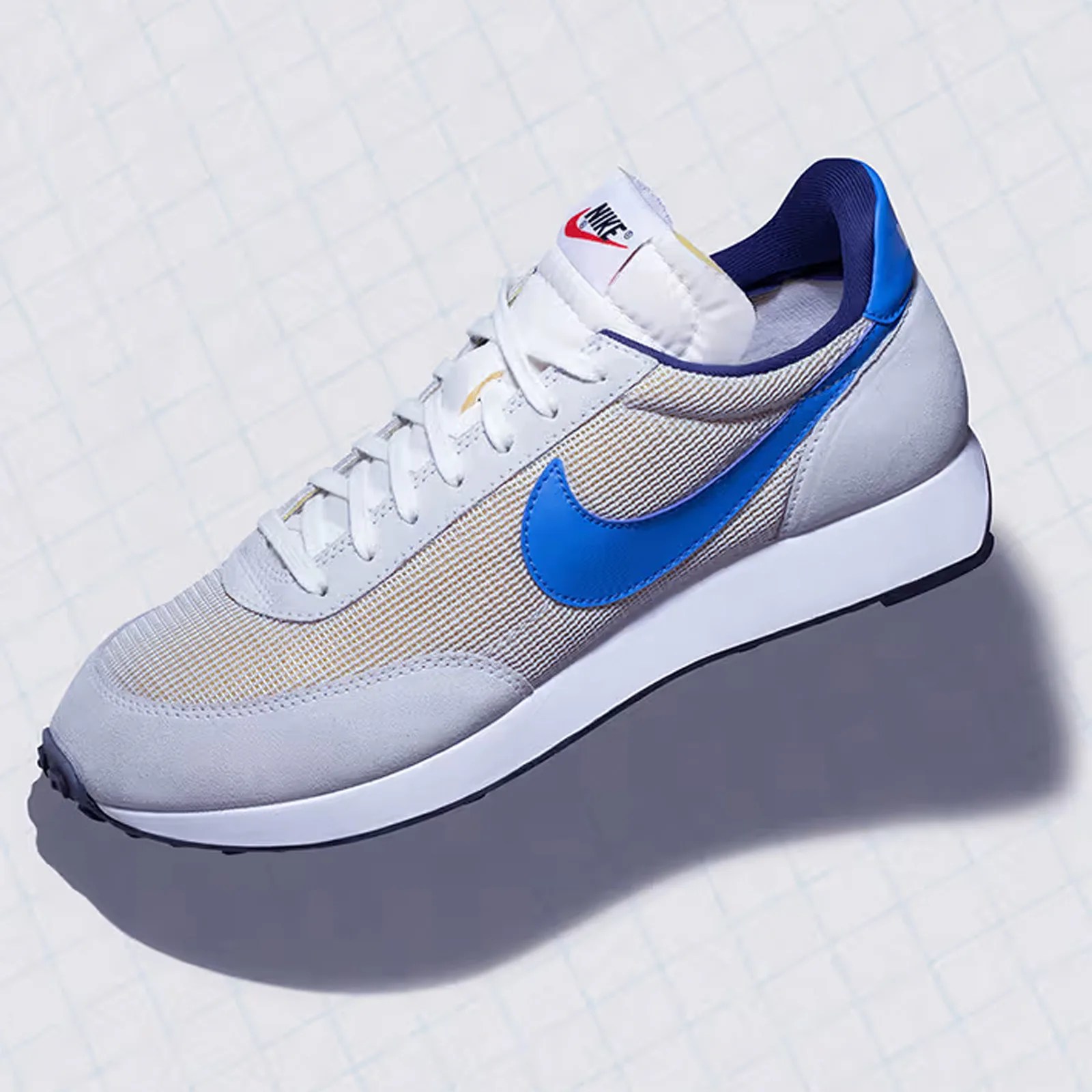 A single Nike AIR TAILWIND 79 sneaker in grey and white with a bright blue check floating above what appears to be a graph paper background. 