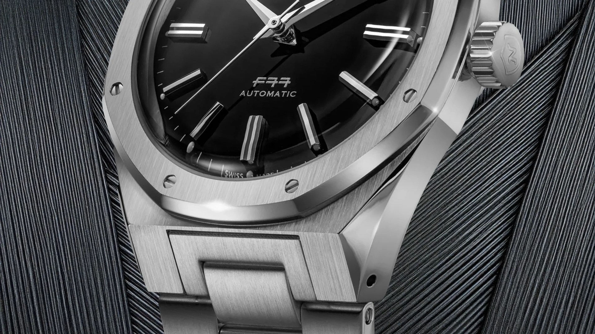 The bottom portion of the The Nivada Grenchen F77 Mark II in stainless steel shown against a metallic background image
