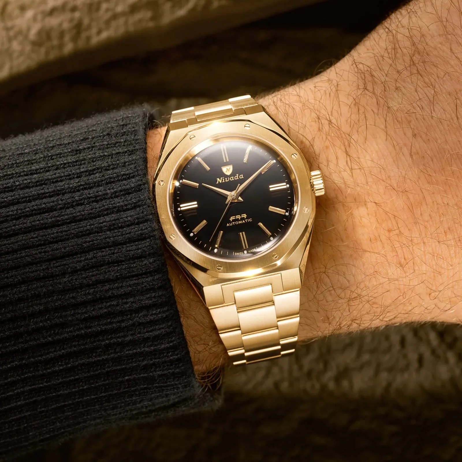 A Nivada Grenchen F77 Mark II Gold shown on a man's wrist wearing a dark black sweater. 