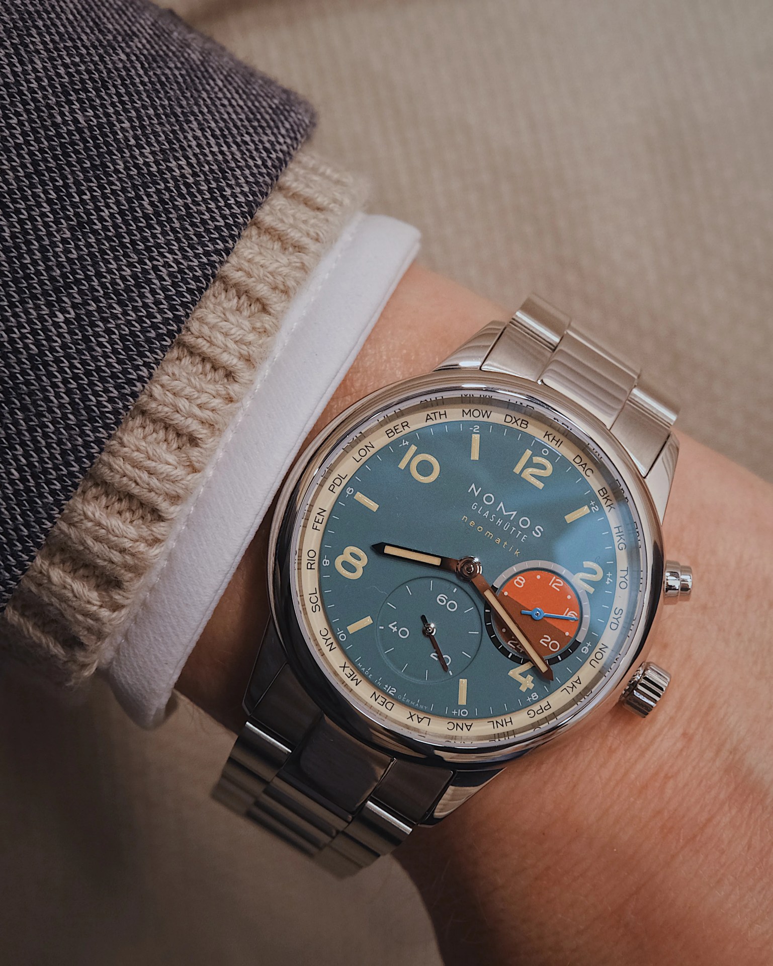 Nomos Club Sport Neomatik Worldtimer shown on the wrist of a male arm. The cuff of a jacket, sweater and shirt are also visible next to the watch