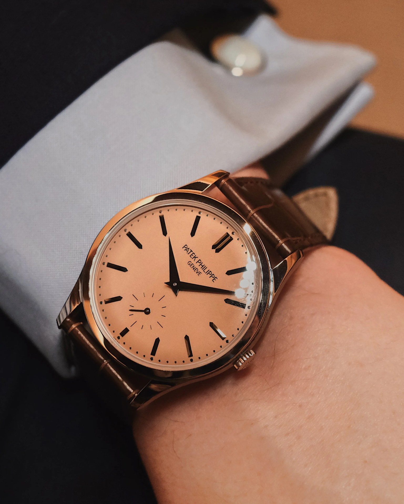 Patek Philippe Calatrava 6169P shown on male wrist against a light blue shirt sleeve and navy jacket.