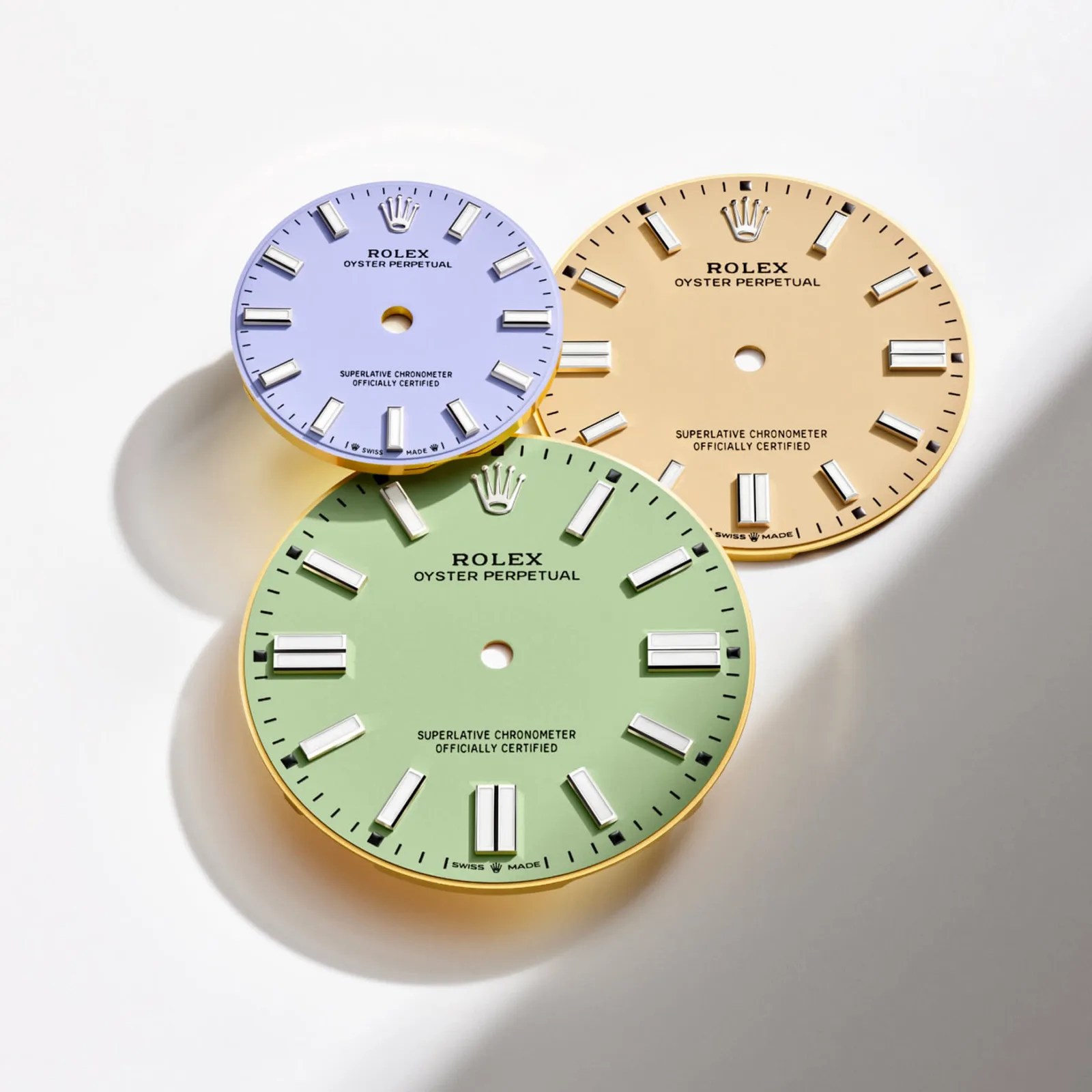 Three new 2025 color dials available on the Rolex Oyster Pepetual shown layered on top of each other against a shadowed white background. 