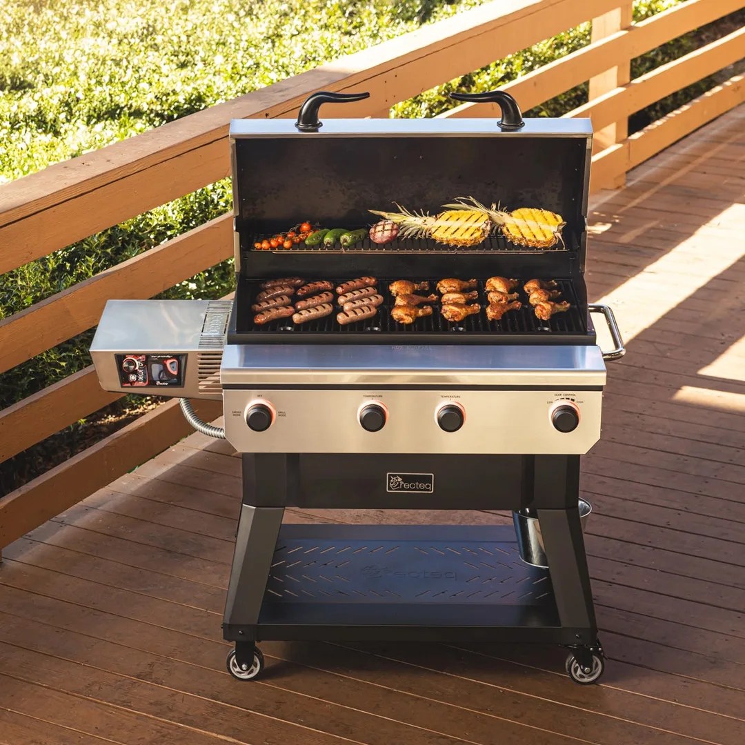 A Recteq X-Fire Pro 825 shownopen with a fully loading grilling surface of meet and veggies on a wooden deck.