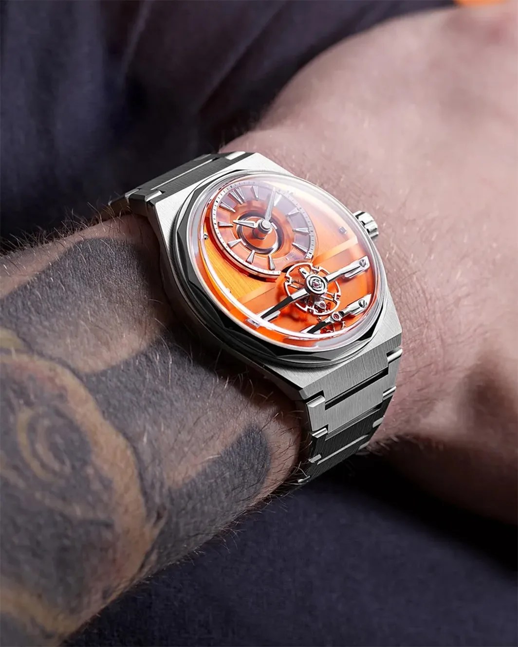 a steel Christopher Ward watch with an orange dial