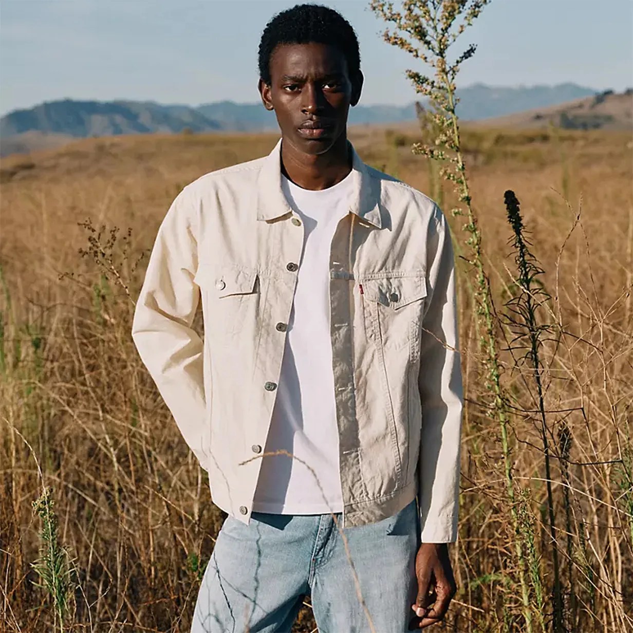 a man in a white trucker jacket and jeans standing in a field