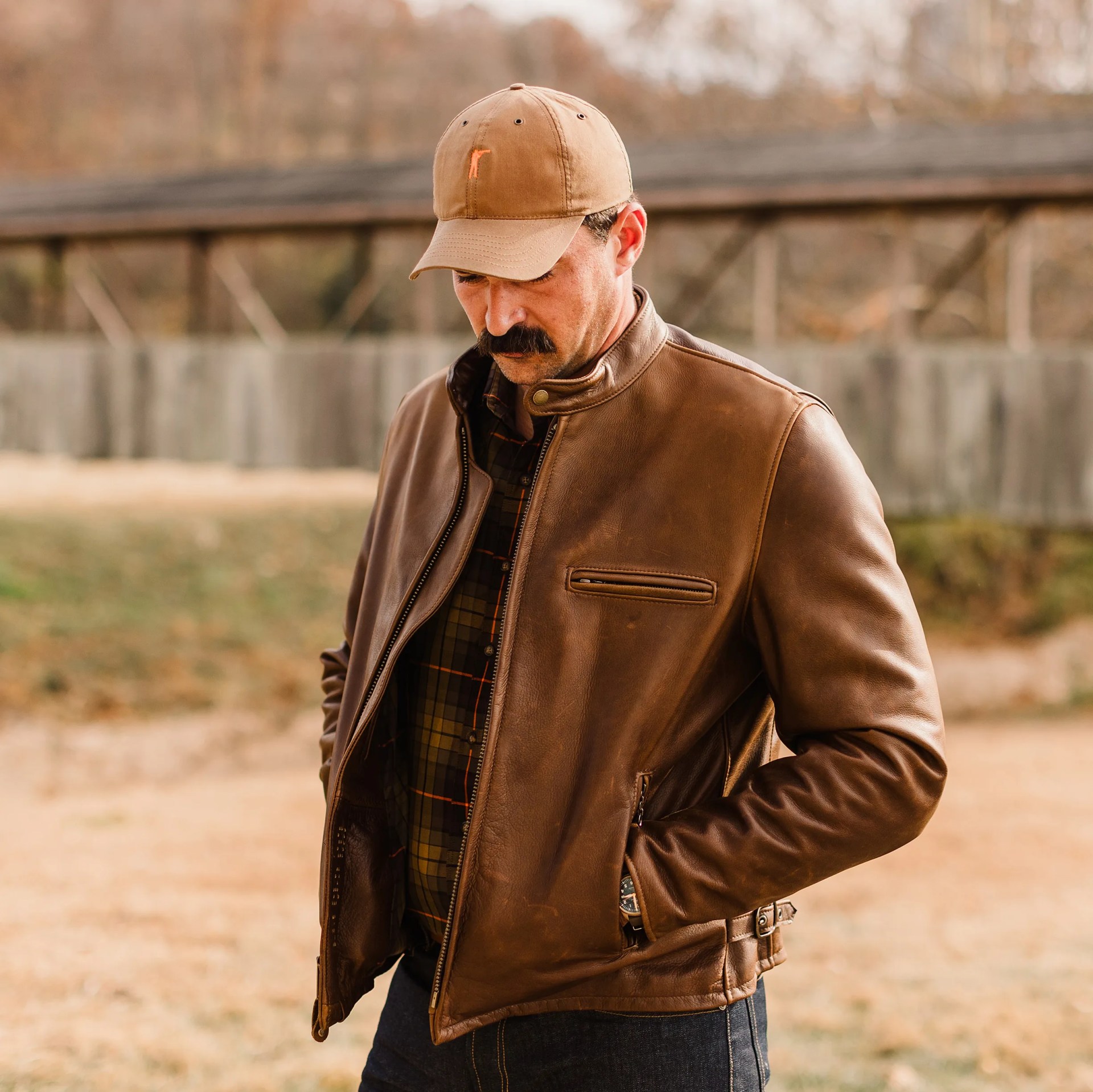 a man in a leather jacket and tan baseball hat