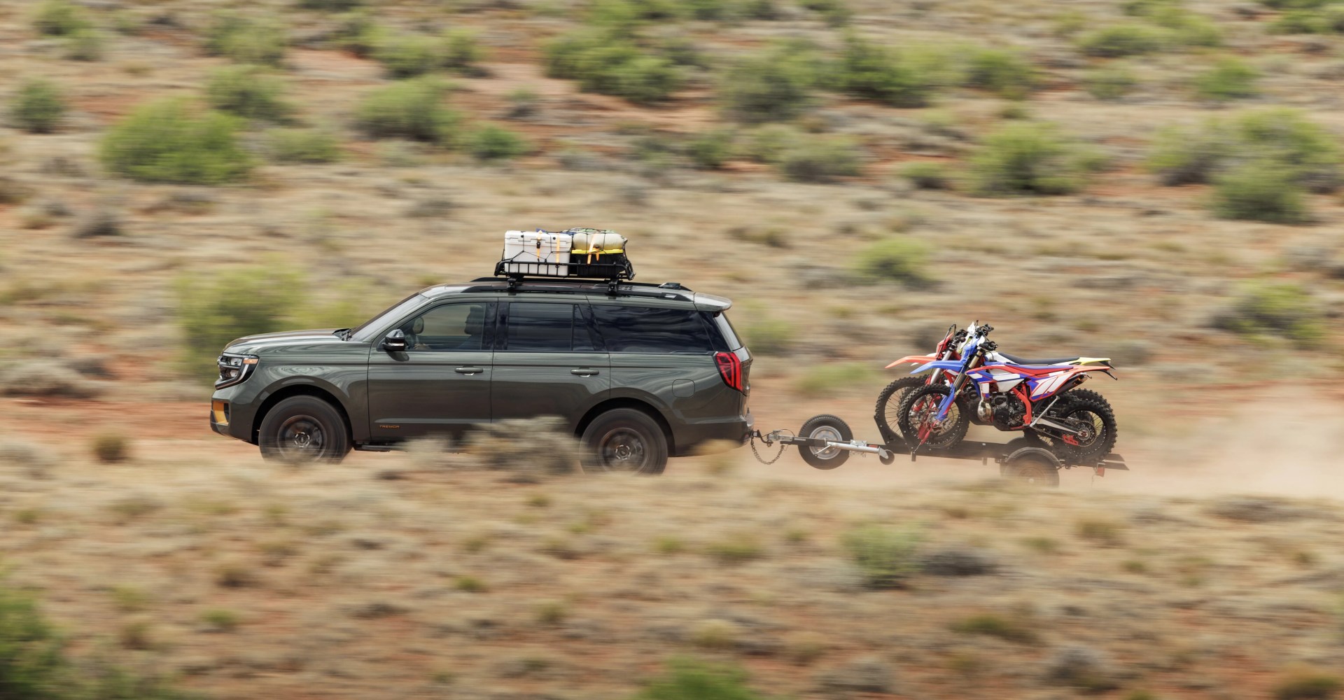 The Ford Expedition Tremor driving through the canyon with a roof rack loaded with gear and a trailer with dirt bikes.