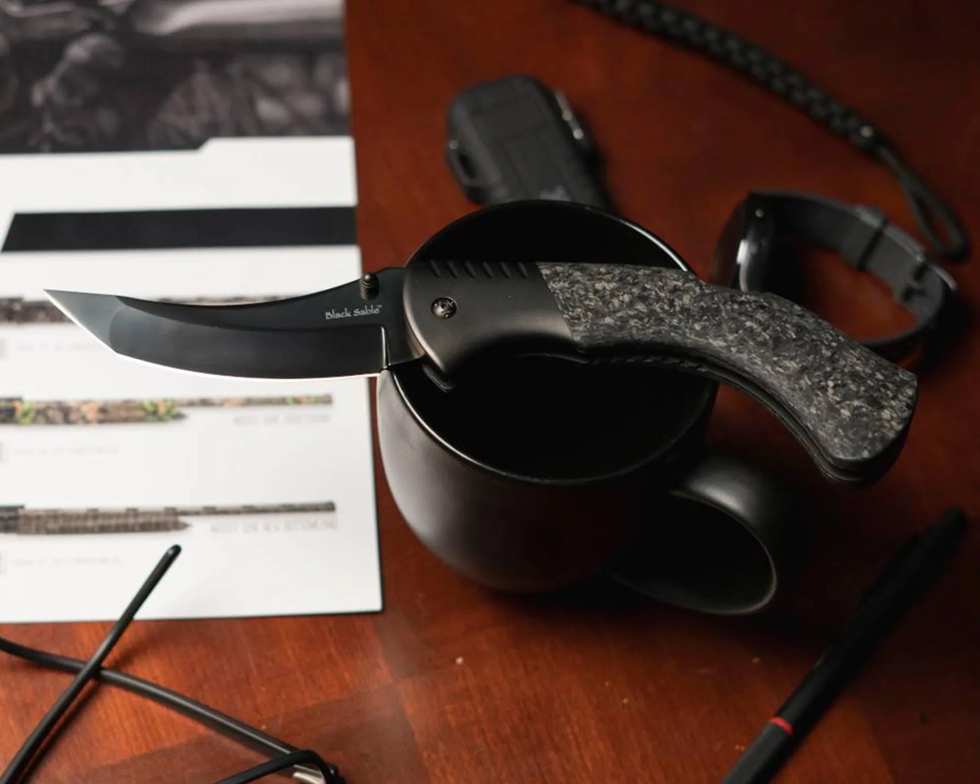 Cold Steel Black Sable EDC Knife on coffee mug on wood desk with watch, glasses, pen, etc.