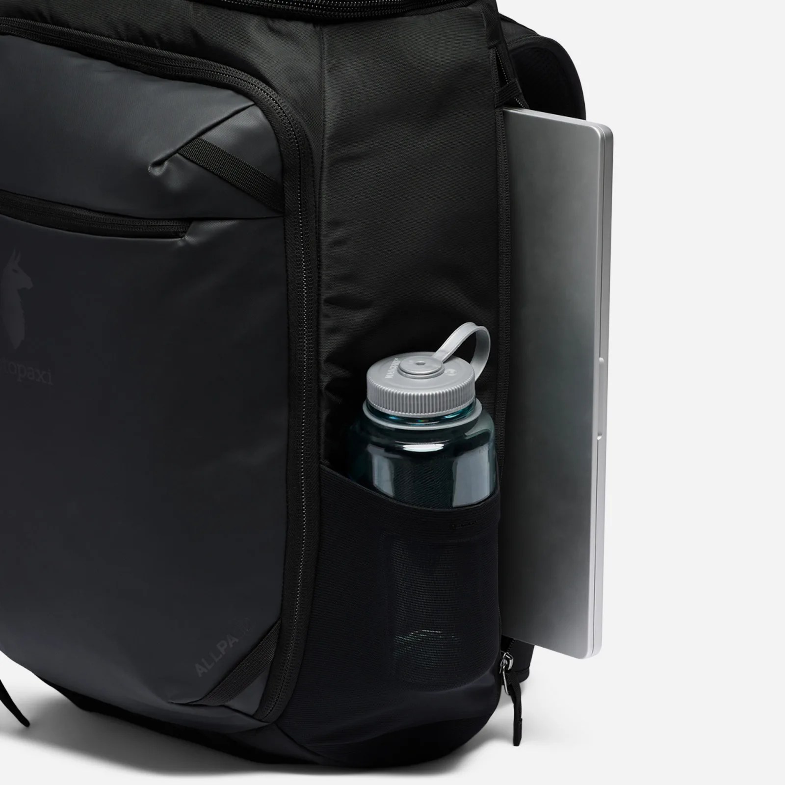 The Cotopaxi Allpa 50L Adventure Travel Pack shown with a laptop sliding out of the back pocket of the bag. A water bottle is also shown sitting in an external sleeve. 