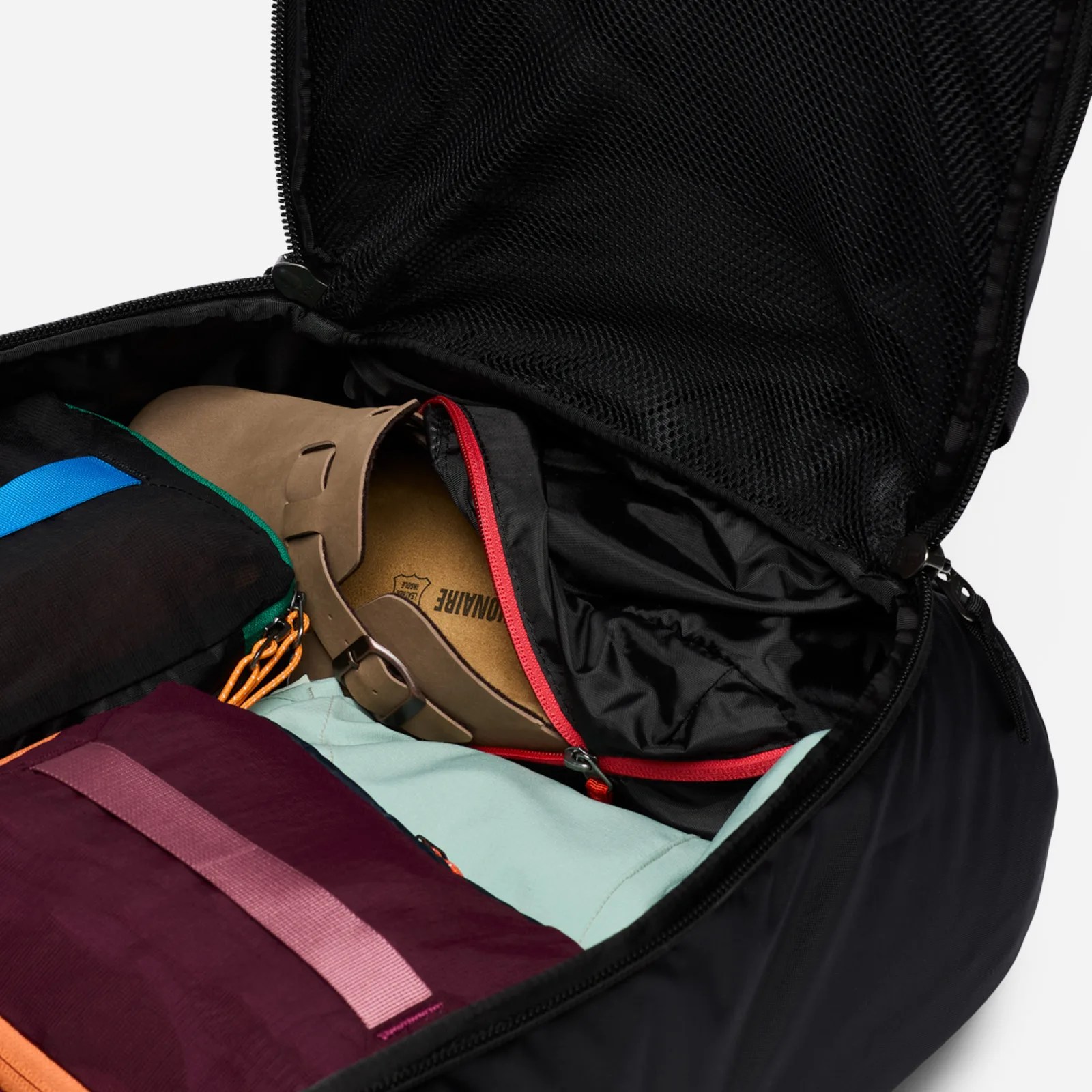 The Cotopaxi Allpa 50L Adventure Travel Pack shown open to reveal packed contents and a bottom zipper pocket