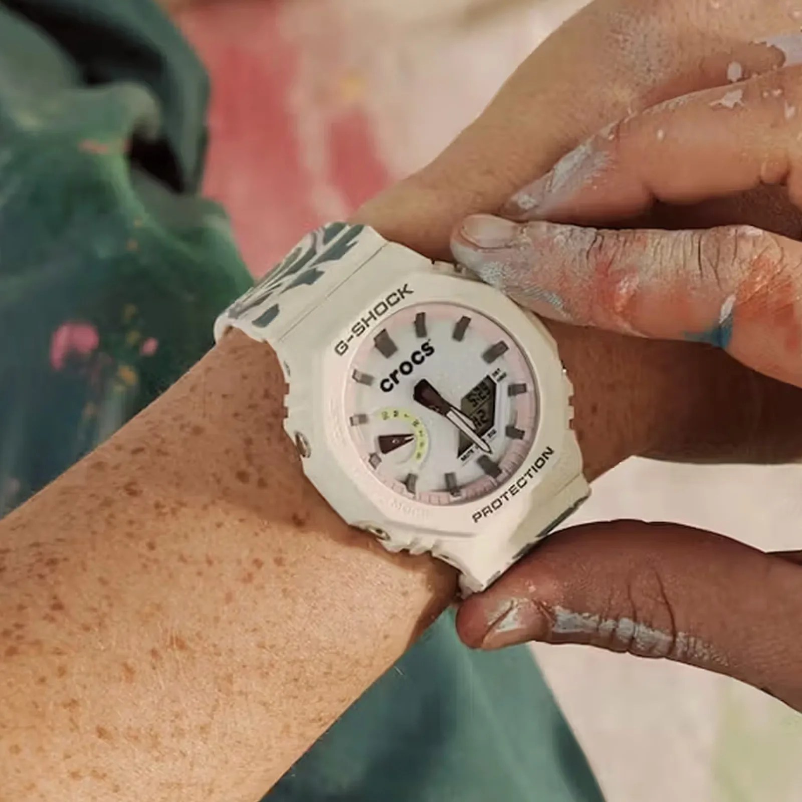 A close-up of the face of the G-Shock x Crocs Echo Wave watch being worn on a wrist with fingers dirty from sculpting / painting pressing the watch's buttons. 