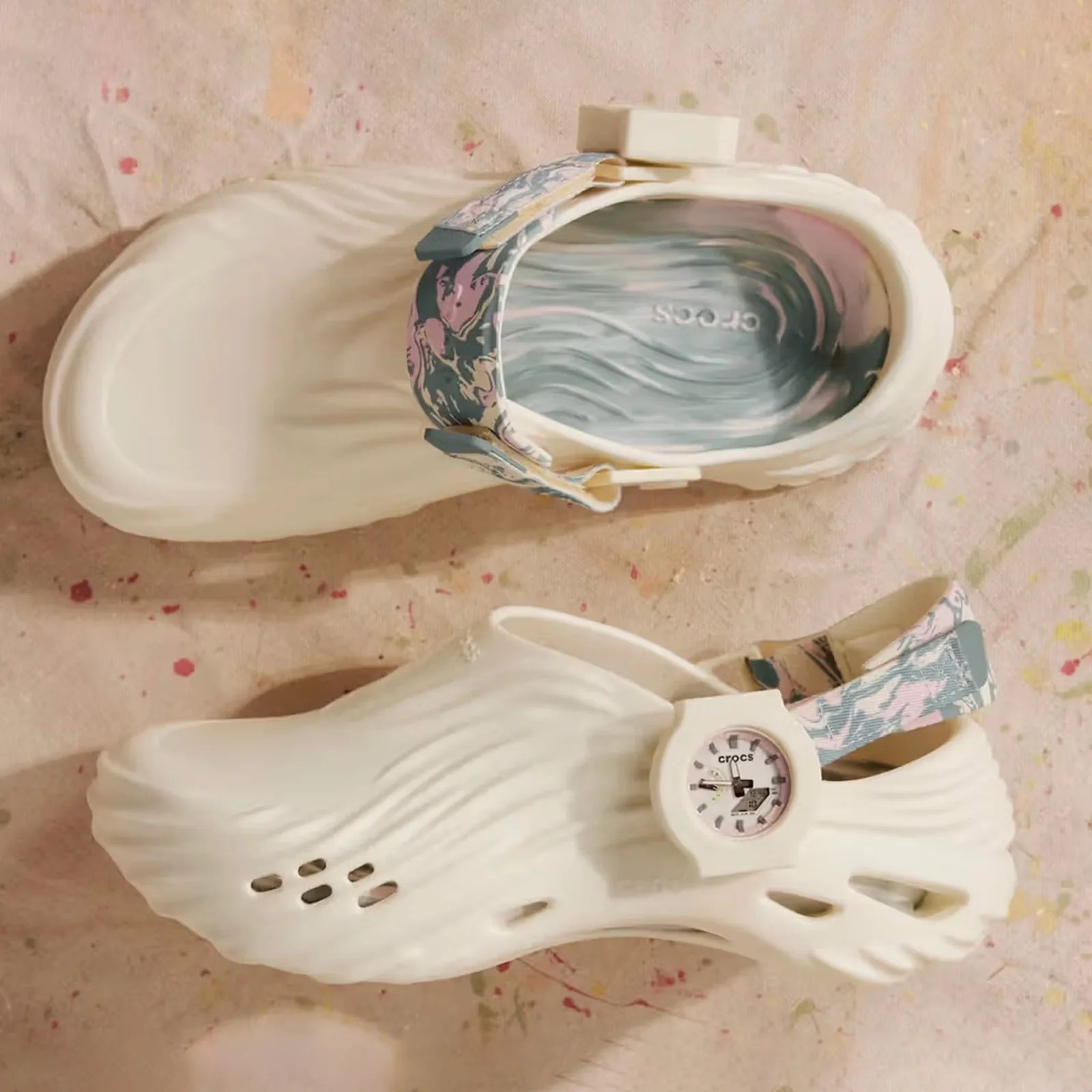 The G-Shock x Crocs Echo Wave Bundle shown in profile and from above lying against a background speckled with colorful paint flecks.