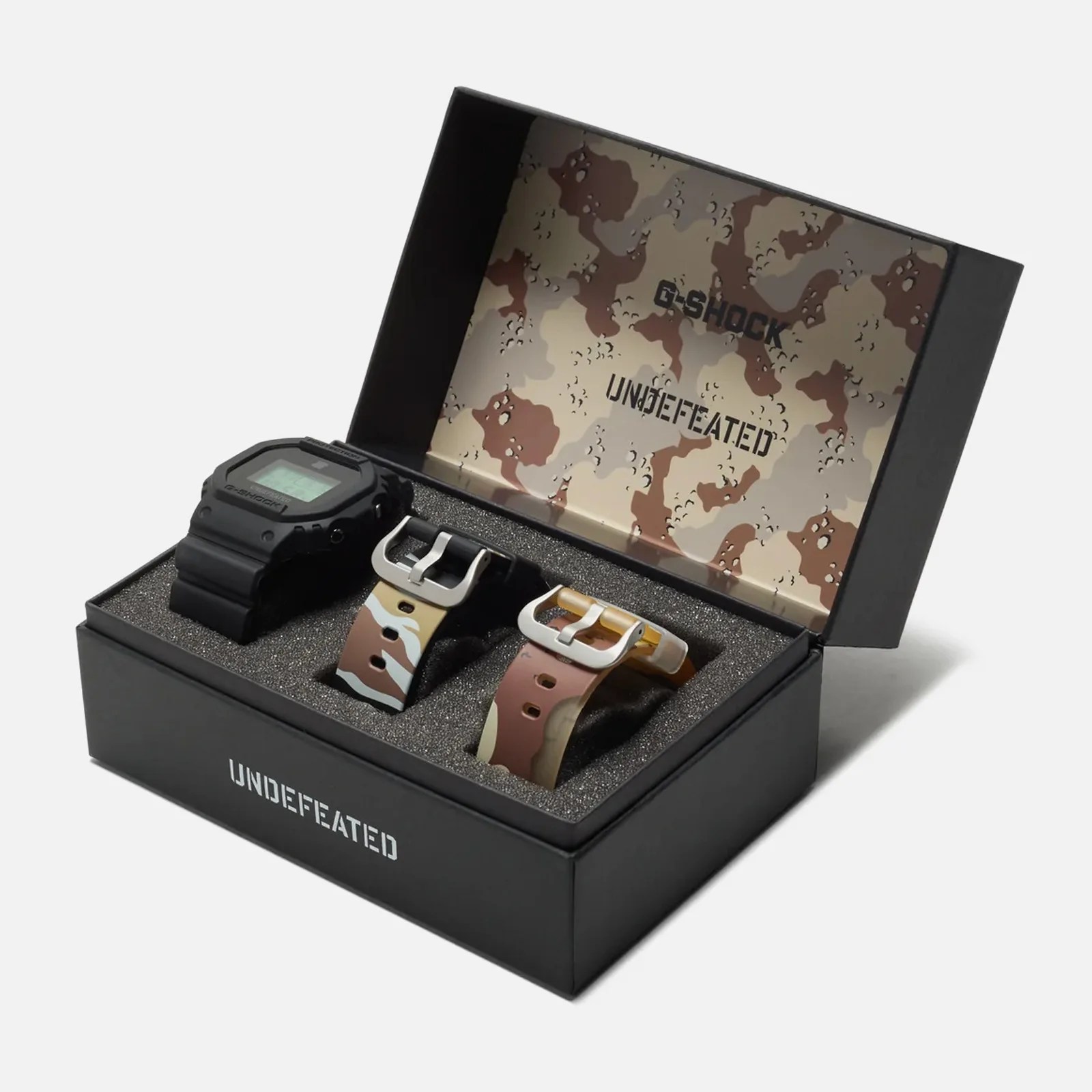 The G-Shock and 'Undefeated' DWE5600UD shown in its presentation box alongside the included two additional camo straps