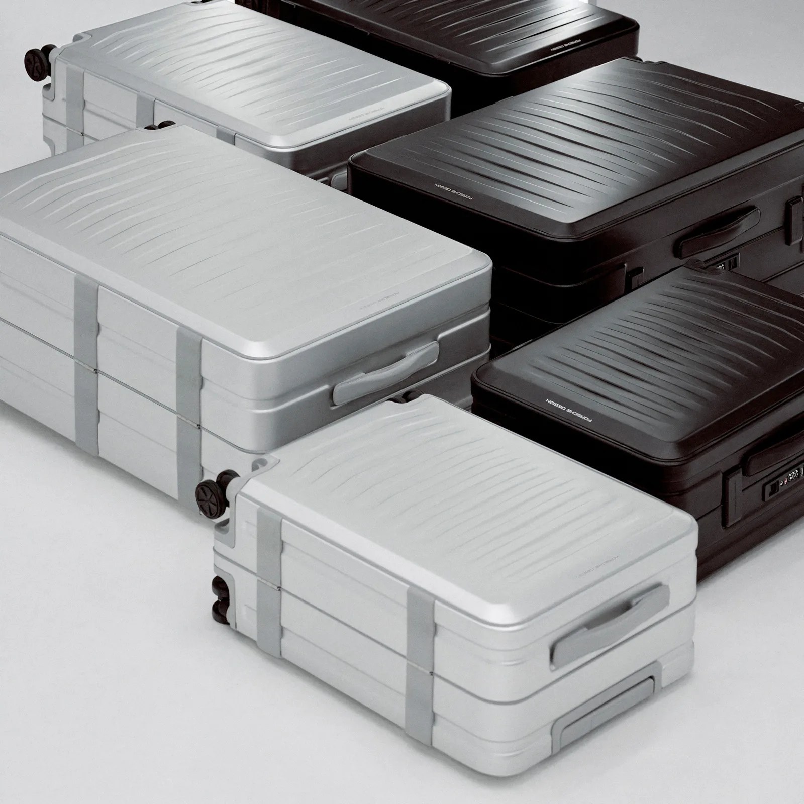Three different silver and black colored versions of the Porsche Design Roadster aluminum suitcase laying flat in a grid on the ground.  