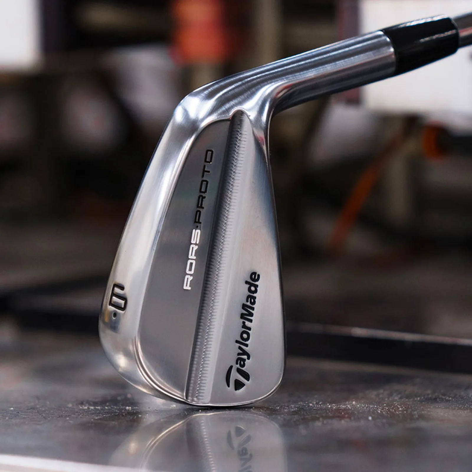 A close-up of the club head of a Taylor-Made RORS∙PROTO Irons made for Rory McIlroy shown resting on a metal work table.
