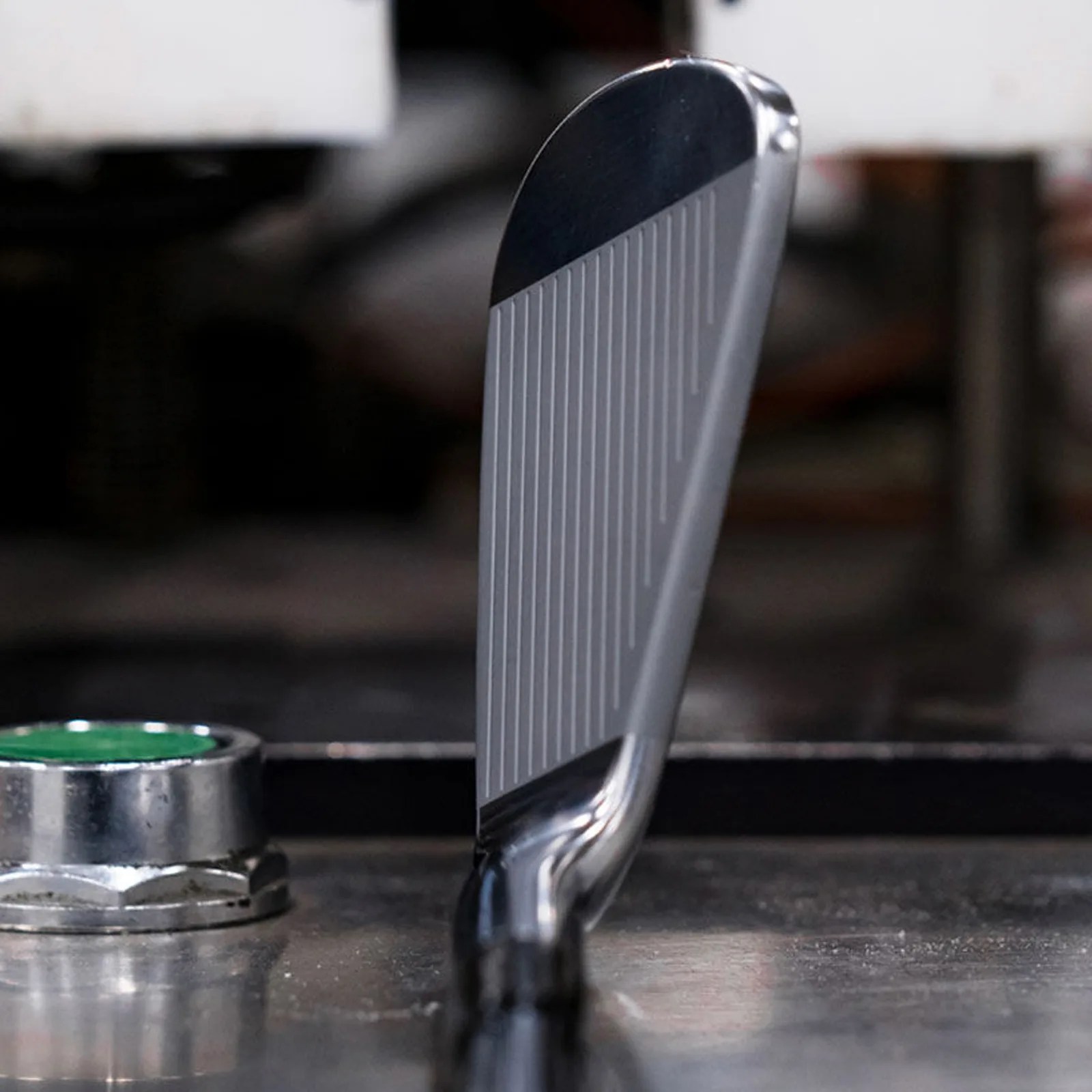 A close-up of the club head of a Taylor-Made RORS∙PROTO Irons made for Rory McIlroy shown resting on a metal work table. 