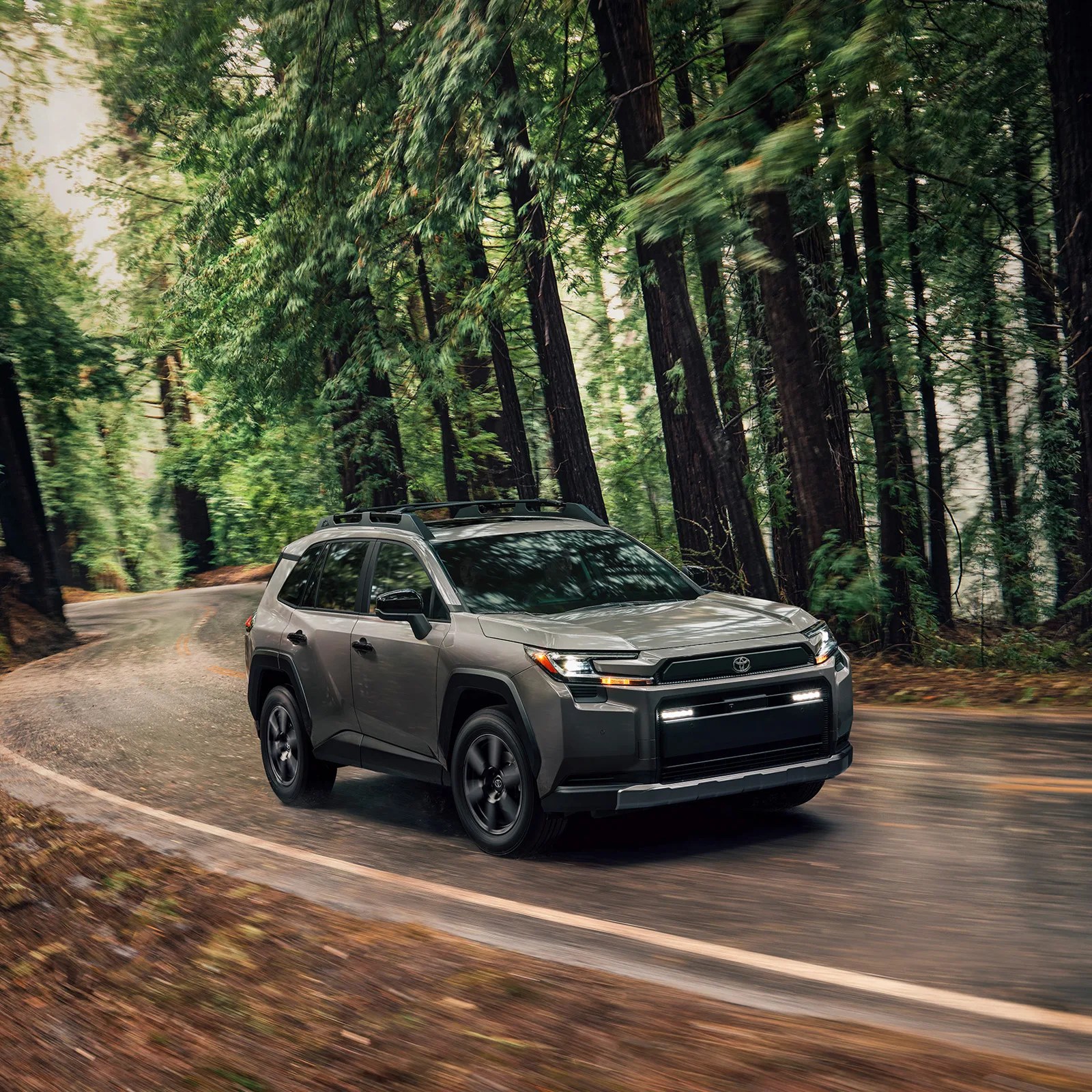 A 2026 Toyota RAV4 Woodland Edition shown driving down an asphalt road in a forest. 