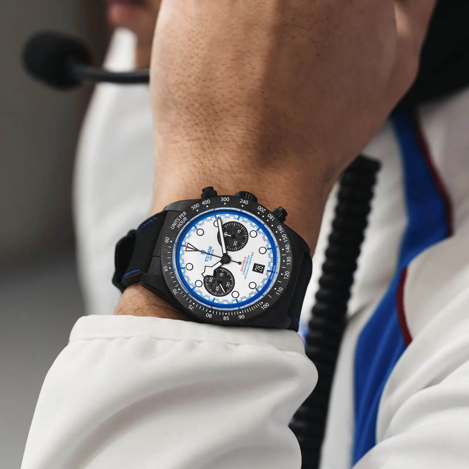 The Tudor Black Bay Chrono "Carbon 25" watch being worn by an F1 racer in a white racing suit. 
