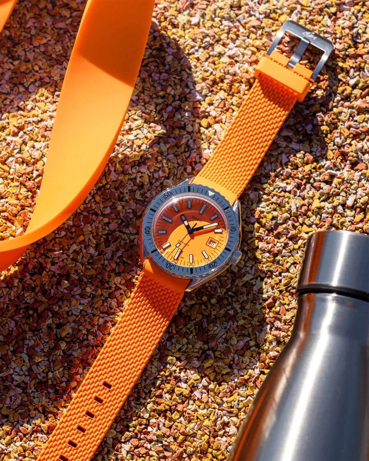 an orange dive watch laying on sand