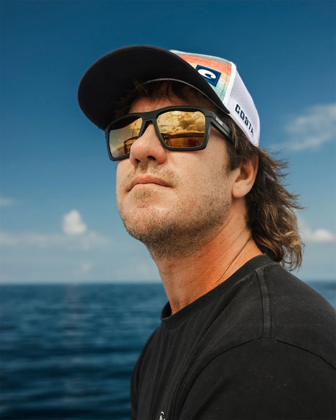 man looking off into distance wearing costa sunglasses with the ocean behind him
